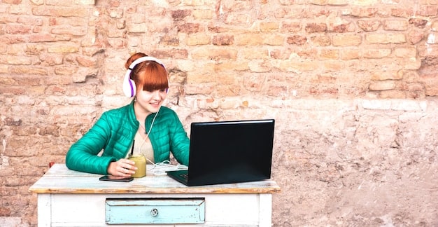 A student wearing headphones and sitting in front of a laptop, with a split screen showing both the original educational material in English and a translated version in another language. The setting is a bright, modern library, conveying a sense of focused learning.